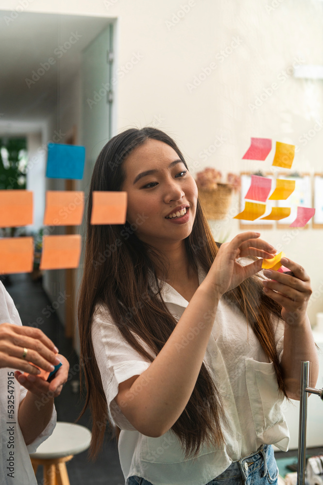 Multiracial businesswomen putting post-it notes on glass board Multiracial businesswomen putting post-it notes on glass board
