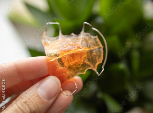 an apparatus for correcting the bite in children, in the hand of a girl, against the background of a houseplant, in daylight. Hygiene, dental treatment, bite correction, new technologies.