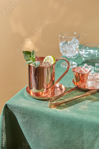 Copper cup of fresh lime drink and tongs for ice. photo