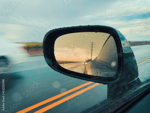 Raindrops on a sport car mirror with reflection of a wet road and power lines in California as a car passes by