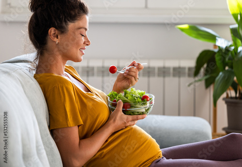 Pregnant woman eating salad on couch photo
