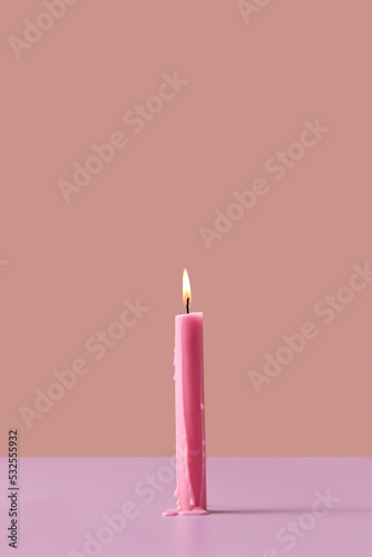 Burning pink candle on pastel background.
