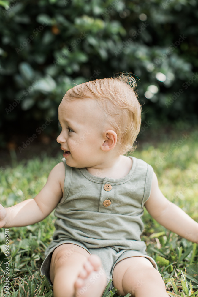 Cute baby boy sitting on the grass turned away Cute baby boy sitting on the grass turned away