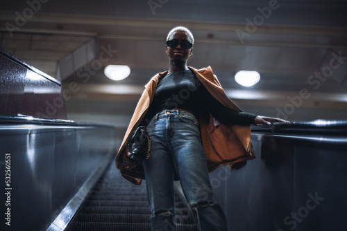 Foto A stylish young black female in a coat and with a clutch is descending using an