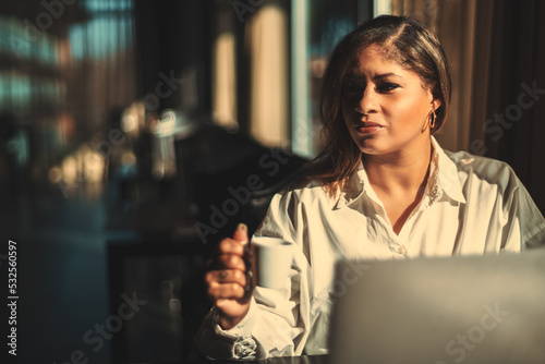 Portrait of a ravishing Hispanic female drinking coffee while using her laptop in a cafe; beautiful adult plus size Brazilian businesswoman having a coffee break; with a copy space place on the left