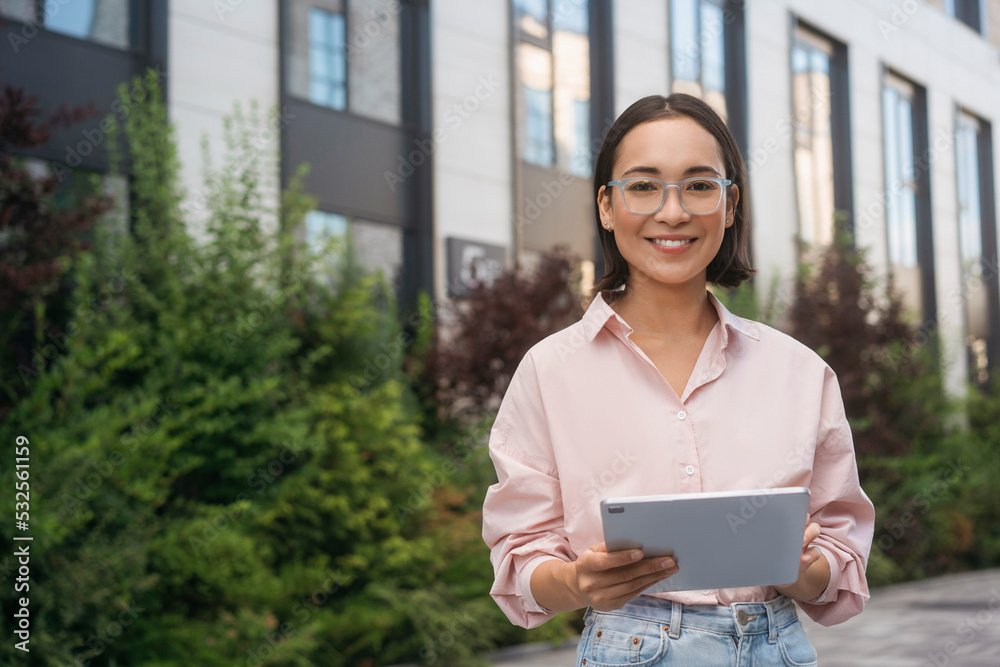 Fototapeta premium Smiling confident asian woman wearing stylish eyeglasses holding digital tablet looking at camera, copy space 