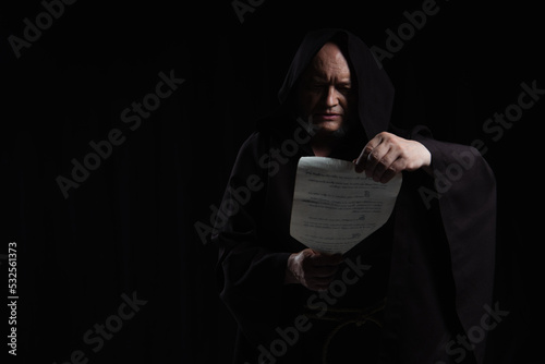 Fotografie monk in hooded cassock reading medieval manuscript isolated on black