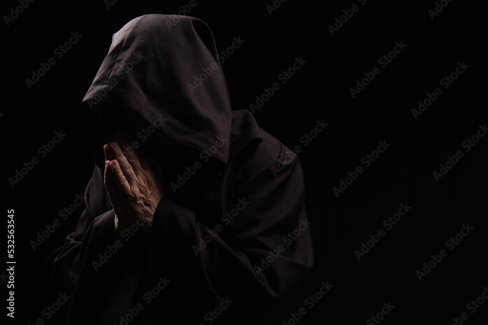 mysterious priest in hooded robe praying isolated on black. - obrazy, fototapety, plakaty 