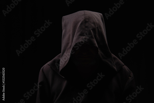 medieval monk with face under dark hood isolated on black.
