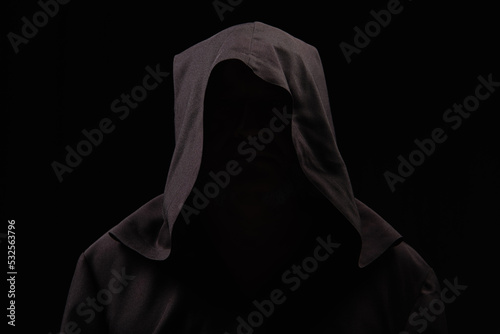 mysterious anonymous monk in dark hood isolated on black.