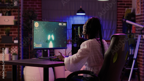 Schilderij op canvas Woman playing multiplayer space shooter simulation enjoying free time using pc gaming setup in home living room