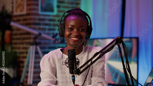Portrait of online radio host smiling confident at camera while broadcasting live using professional equipment in recording studio. African american podcaster sitting at desk with boom arm microphone.