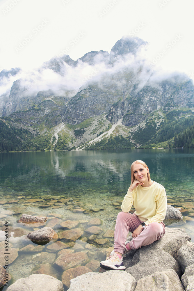 Poland - September, 2022: beautiful blonde sits on the background of the lake Morskie oko