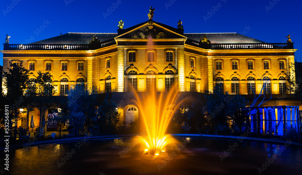 Scenic summer night view of illuminated Opera-Theatre de Metz Metropole surrounded by green park with fountain in front of majestic building, France..