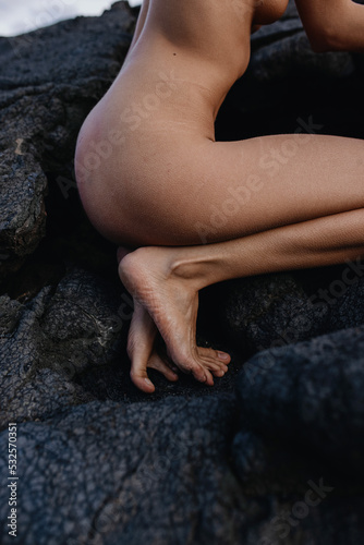 Nude woman squatting on black solid lava in Iceland 