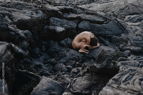 Nude woman sitting in fetal position on black solid lava in Iceland  photo