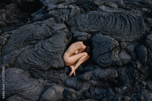 Nude woman lying in fetal position on black solid lava in Iceland  photo