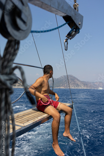 Smiling young man sitting on sail boat and fishing. 