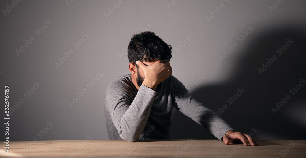 Obraz premium A man sits in front of a table covering his face with his hand