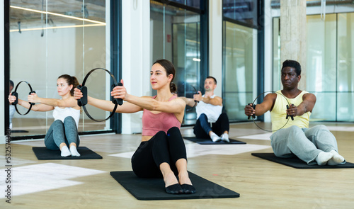 Group of young adults maintaining active lifestyle exercising with flexible ring during pilates class in modern fitness center