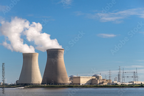 Antwerpen, Flanders, Belgium - July 10, 2022: Landscape, Cooling towers blowing steam in blue air in evening, and Doel Nuclear Power plant buildings, seen from Scheldt river