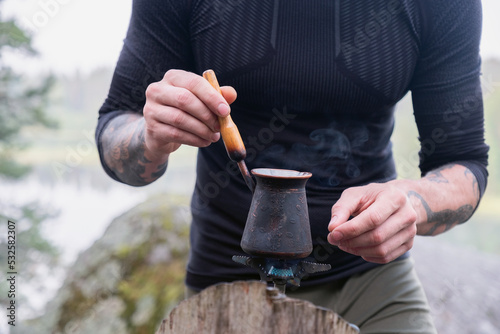 Aman makes coffee in a turk on a rock in the forest