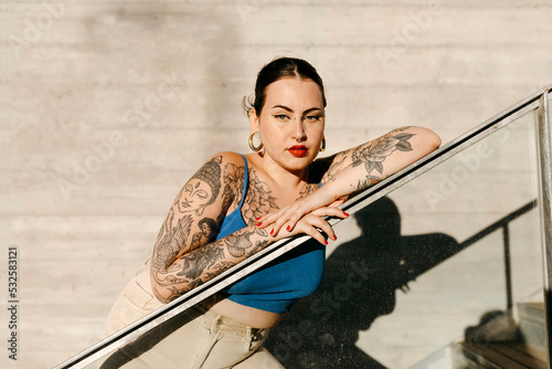 Curvy tattooed woman leaning on railing in city