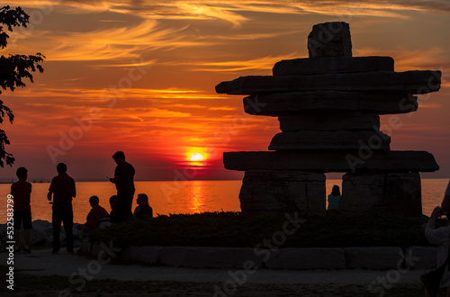 Silhouette of people watching the sunset on the shore of waterfront park with Inukshuk photo