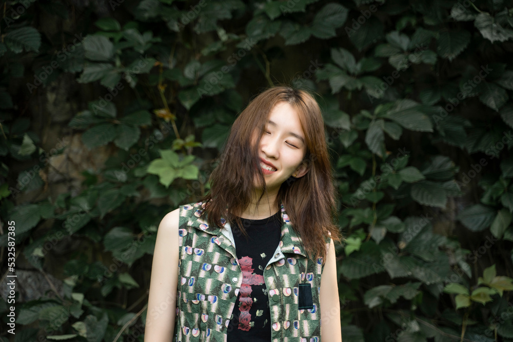 young woman is in front of the green plant wall young woman is in front of the green plant wall