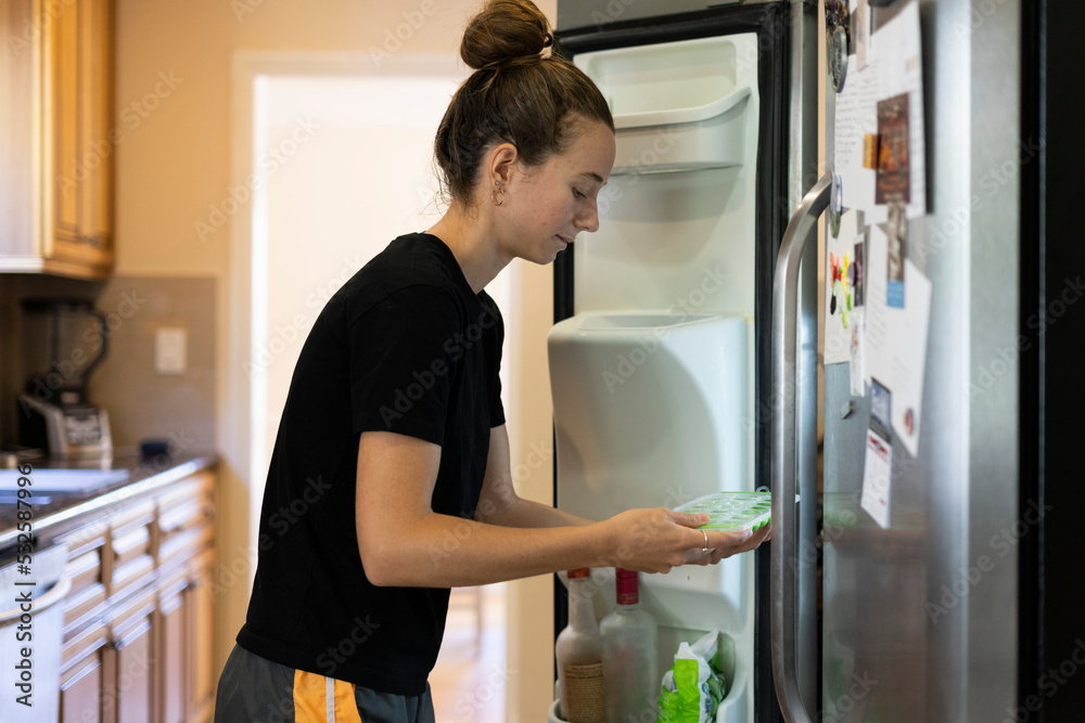 Young woman replaces an ice cube tray at home in the morning Young woman replaces an ice cube tray at home in the morning