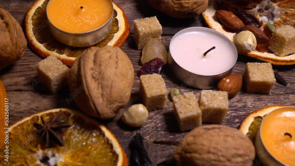 Natural composition in hygge style with candles, orange slices, fragrant spices, walnuts and pine cones on an old vintage wooden board background.