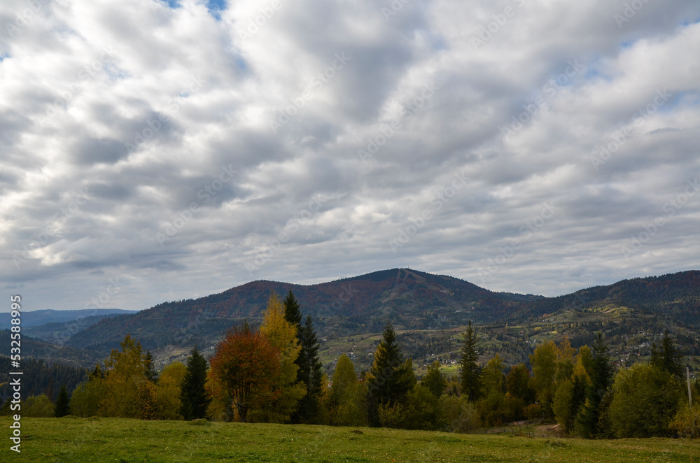 Scenic view of autumn trees against mountains under cloudy sky. Carpathian Mountains, Ukraine 