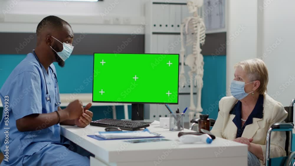 Nurse looking at greenscreen display with paralyzed patient in wheelchair at checkup visit. Assistant using isolated chromakey copyspace and mockup template, disability. Tripod shot.