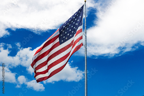 Large American flag waving in the wind against a cloudy blue sky.