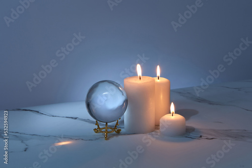 Magical glass ball with burning candles in dark photo