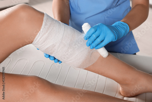 Tableau sur toile Doctor applying bandage onto patient's shin in hospital, closeup