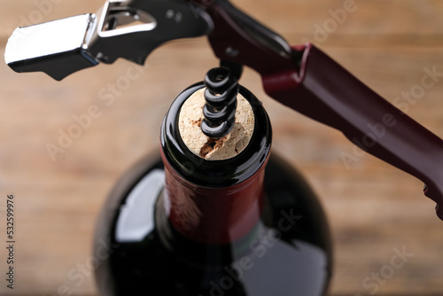 Opening wine bottle with corkscrew on blurred background, closeup