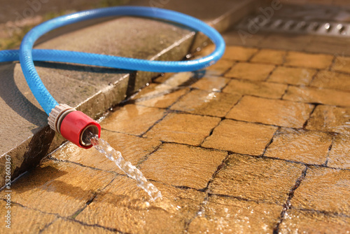 Water flowing from hose on stone floor outdoors, closeup. Space for text
