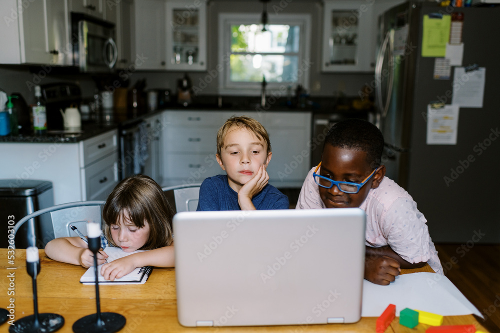 Three children sitting at the kitchen table looking at a laptop Three children sitting at the kitchen table looking at a laptop