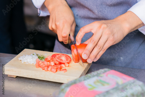 Hands of an unrecognizable person cutting tomato, chili and onion on a board.