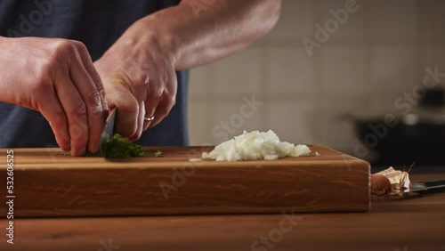 A male home chef making Bulgarian moussaka in his kitchen. Closeup shot - chopping fresh parsley on a wooden cutting board.