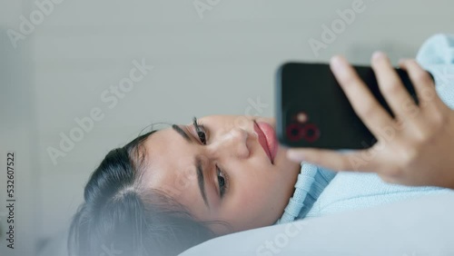 Stress, headache and anxiety by woman texting on phone, reading message and lying on a bed in her home. Anxiety, bad news and sad girl suffering with mental health problem and migraine while browsing photo