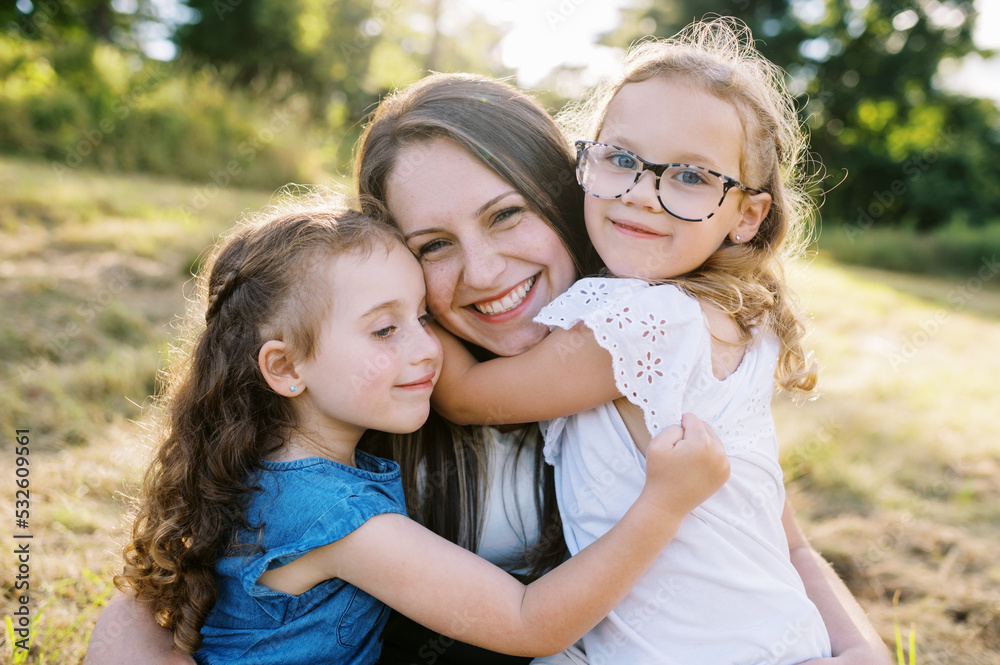 Portrait of a mother and her two daughters sitting down in a field Portrait of a mother and her two daughters sitting down in a field
