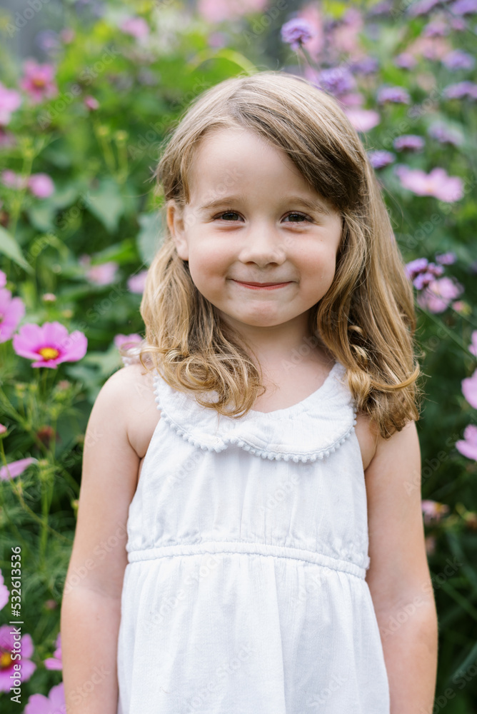little toddler girl in white dress playing in the grass by flowers little toddler girl in white dress playing in the grass by flowers