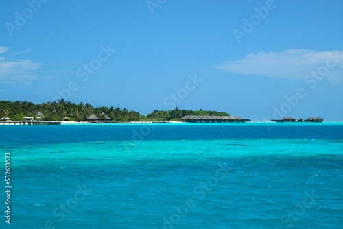 Turquoise water in the Maldives, resort bungalows with thatched-roofs, crystal clear water, blue skies and vegetation 