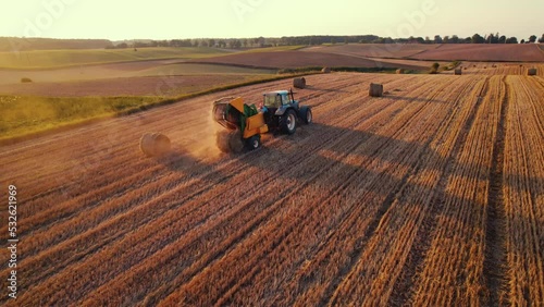 Golden field with bales of hay and blue tracktor stacking hay with green fields in the background. Agriculture. Horizontal shot. High quality 4k footage