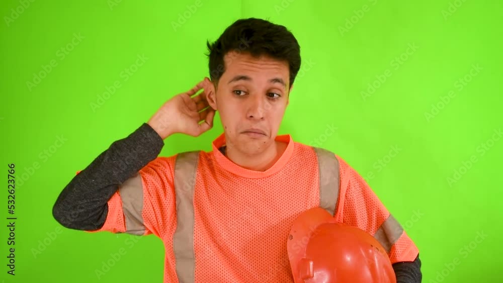 Hombre joven caucasico con uniforme de obrero confundido en una pantalla verde Hombre joven caucasico con uniforme de obrero confundido en una pantalla verde
