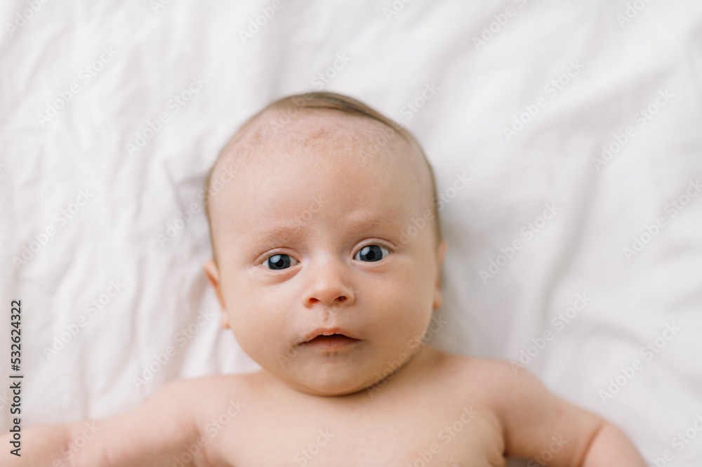Infant baby boy on a white bed with eyes open Infant baby boy on a white bed with eyes open