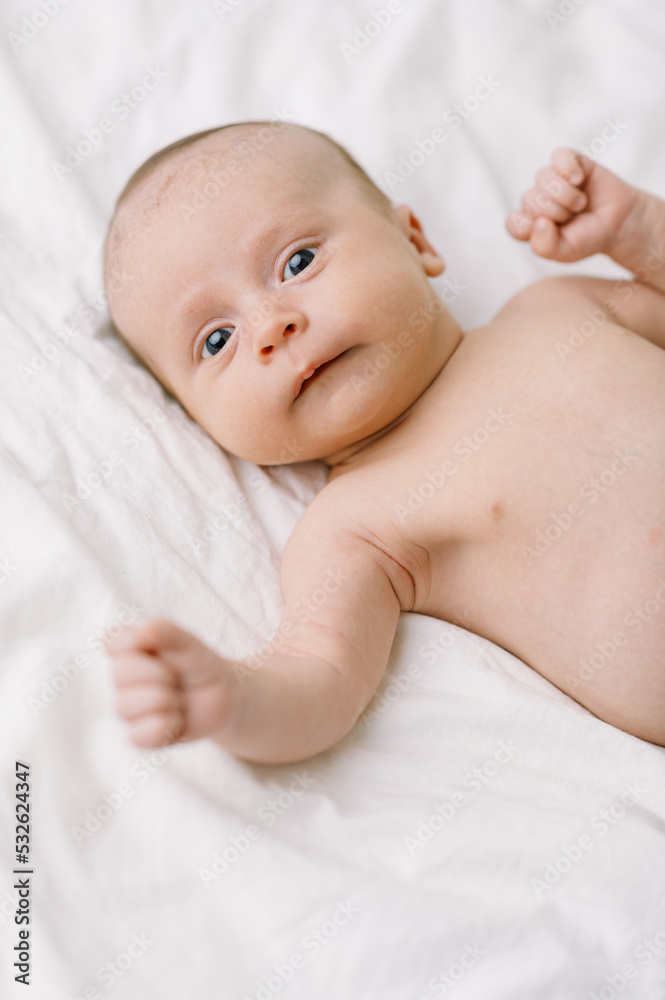 Infant baby boy on a white bed with eyes open Infant baby boy on a white bed with eyes open