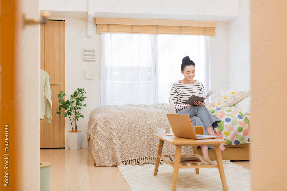 ベッドに座り本を読む若い女性 ベッドに座り本を読む若い女性